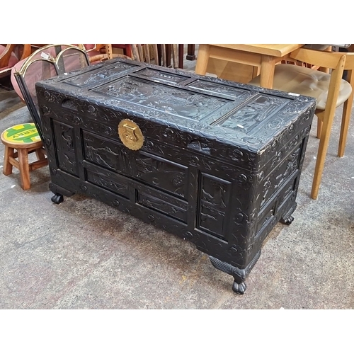 Star lot :An Intricately carved oriental wooden chest with brass detailing, featuring landscape motifs. Hinged lid reveals spacious interior storage.