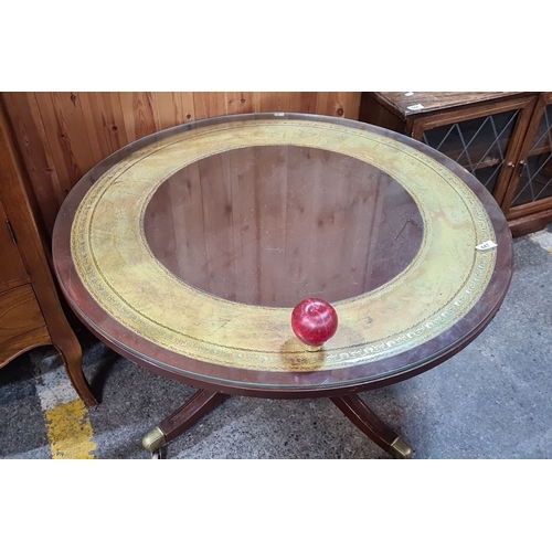 447 - Vintage round glass-top coffee table with brass casters and decorative inlaid tooled leather interio... 