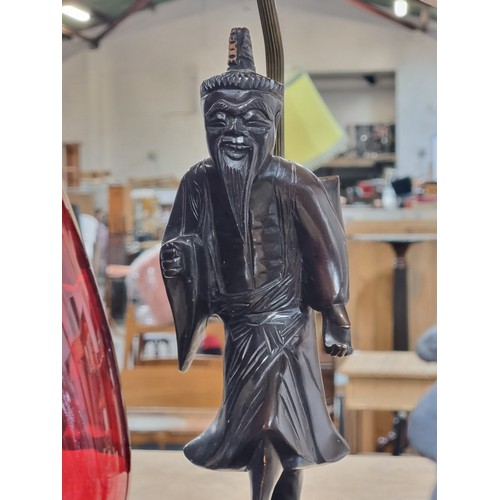 201 - A carved Chinese rosewood and brass table lamp. Features a wise man and velvet trimmed lampshade. Re... 