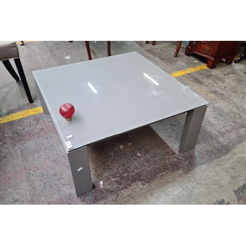 1077 - Coffee table with glass top and metal legs, 90 cm square. It has a glossy surface and sturdy build.
... 