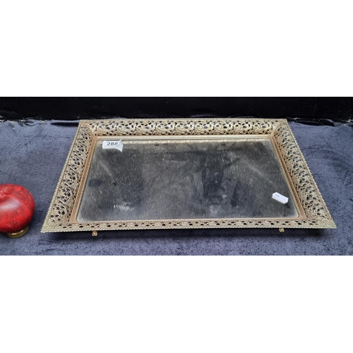 288 - A lovely mirrored serving tray, adorned with intricate gilt detailing along its edges and supported ... 