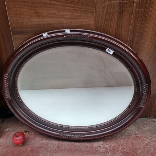 303 - A large oval mirror housed in a wooden frame. MM: 90cm x 70cm.