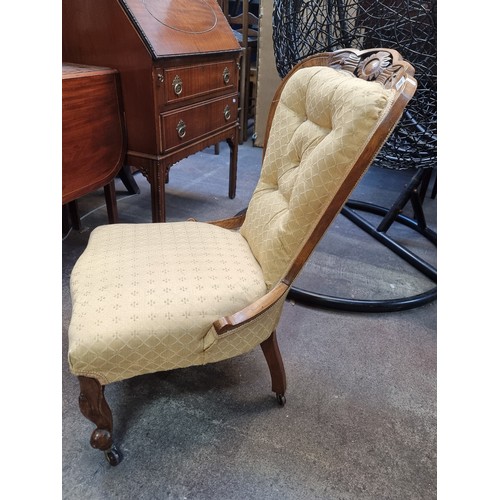 367 - An antique nursing chair featuring a carved oak wood frame, button back with braiding mounted on cas... 