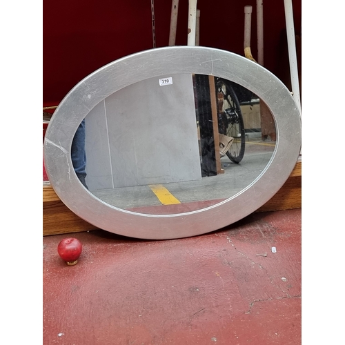 310 - A stylish oval wall mounted mirror housed in a silver gilt frame.