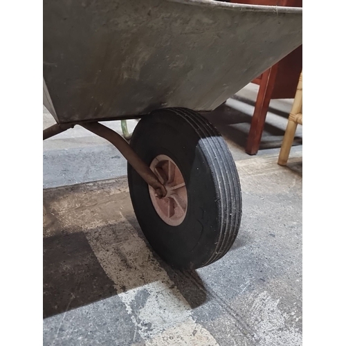 604 - A galvanized metal wheelbarrow with a sturdy steel frame, rubber wheel, and wooden handles.