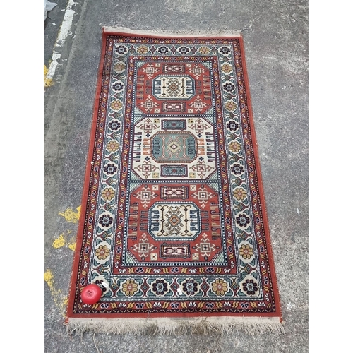 881 - A Persian-style rug, vibrant geometric and floral motifs, rich red and bone tones, fringed edges. 
M... 