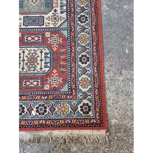 881 - A Persian-style rug, vibrant geometric and floral motifs, rich red and bone tones, fringed edges. 
M... 