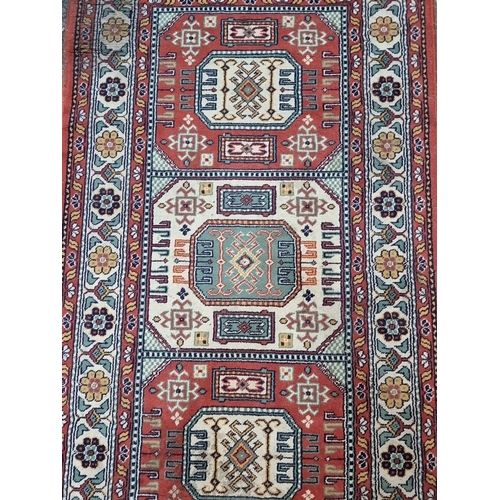 881 - A Persian-style rug, vibrant geometric and floral motifs, rich red and bone tones, fringed edges. 
M... 