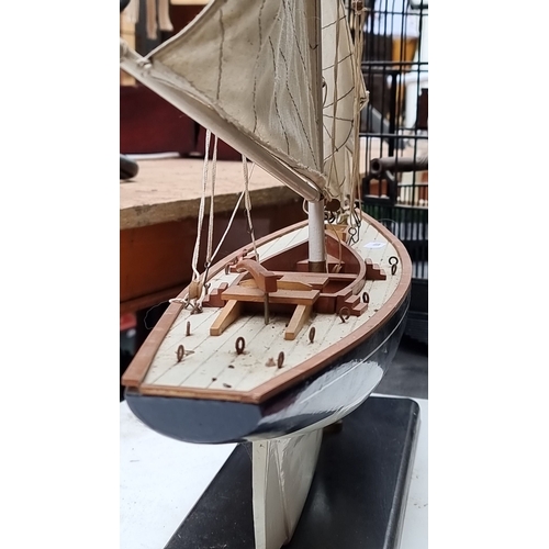 442 - A large Wooden sailboat model on a black stand. Features detailed rigging, cloth sails, and realisti... 