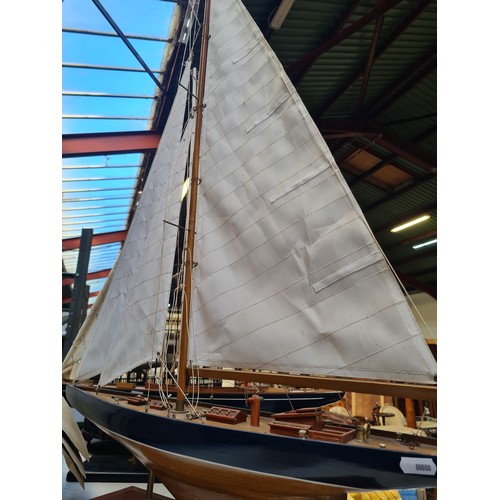 441 - A large Wooden sailboat model features detailed rigging and deck, mounted on a display stand. Approx... 