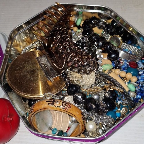 425 - A tin filled with assorted  jewelry, watches and I can see a compact, unchecked.