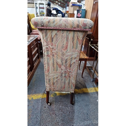 671 - Victorian nursing chair features a high upholstered back, patterned fabric, turned mahogany legs, an... 