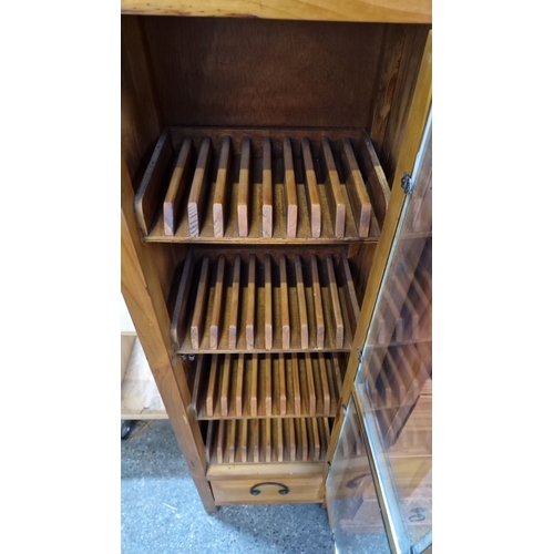 681 - Wooden CD cabinet with glass-paneled door, slotted shelves, and lower drawer.