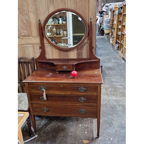 1174 - An Early 20th-century mahogany dressing table with an oval swivel mirror, three drawers, and brass h... 