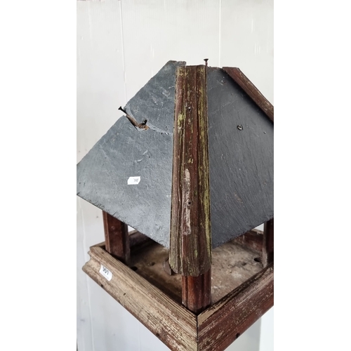 901 - A Rustic wooden bird table with a weathered slate roof. Sturdy, freestanding design.