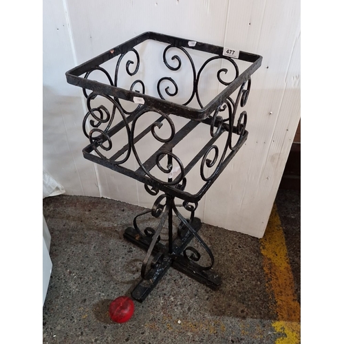 477 - Wrought iron plant stand features decorative scrollwork, square basket design, and tripod base.