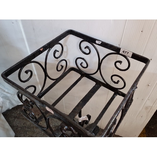 477 - Wrought iron plant stand features decorative scrollwork, square basket design, and tripod base.