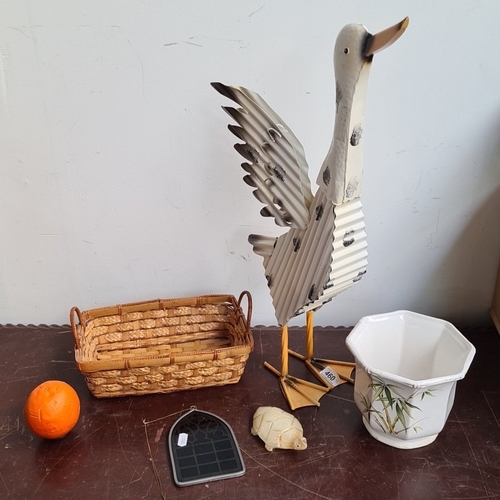 Group of 6 decorative items: corrugated metal goose sculpture, woven wicker basket, octagonal ceramic cachepot with bamboo motif, small soapstone turtle, arched metal-framed glass panel, and an orange decorative sphere.