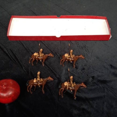 A set of four vintage hand-painted cast metal W. Britain, Indian Lancer cavalry figures, each mounted on a brown horse and carrying a lance, in plain red presentation tray.
