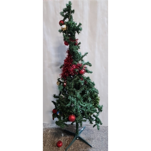 Artificial PVC Christmas tree on green plastic stand, trimmed with red tinsel, metallic bead garlands and assorted glass and plastic baubles.