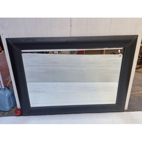 A very large beveled wall mirror. Housed in a leather style frame with cream border stitching. 
MM: 112 cm height x 80 cm width including frame
