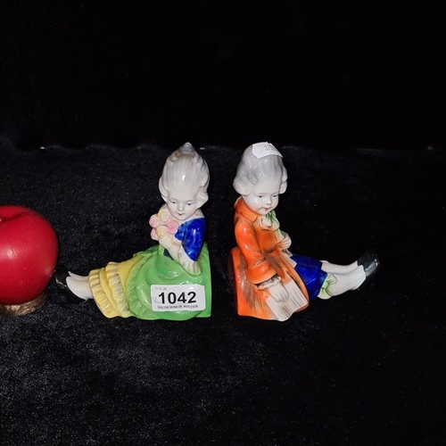Pair of hand-painted porcelain figurines depicting a Rococo-style boy reading and girl holding flowers, each on a coloured plinth and underside stamped “FOREIGN”, likely Continental, early 20th century.