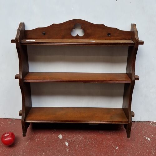 447 - A wooden wall-mounted shelf rack with three graduated tiers, shaped side supports, and a pierced tre... 