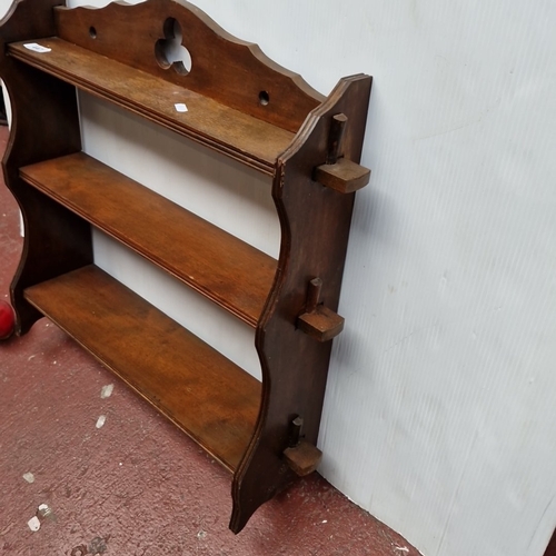 447 - A wooden wall-mounted shelf rack with three graduated tiers, shaped side supports, and a pierced tre... 