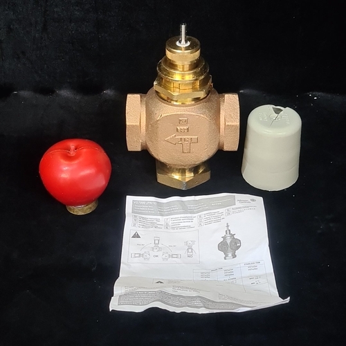 Johnson Controls brass three-way control valve, VG7000 series (PN16), with threaded ports and actuator spindle, accompanied by a red handwheel and plastic protective cap; the body cast with CE mark and directional arrow.