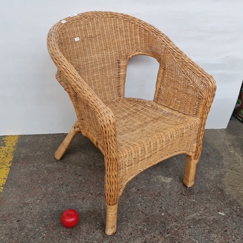 Wicker armchair of tub form, the arched back centred by an openwork handle, with woven seat, scrolling arms and braided rim, raised on splayed legs with X-form stretcher, the underside with board seat support.