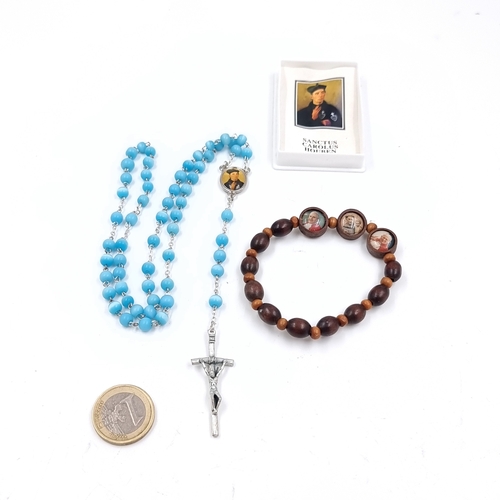 A vintage boxed set of Blue Glass Rosary beads and a metal crucifix. Centre of crucifix depicts blessed Carlow Acutis. Lot also includes a A vintage wooden Rosary bracelet with three sacred portraits honouring three Canonized modern popes. Bracelets holds photos of John Paul II, Saint Paul VI, St. John XXIII.