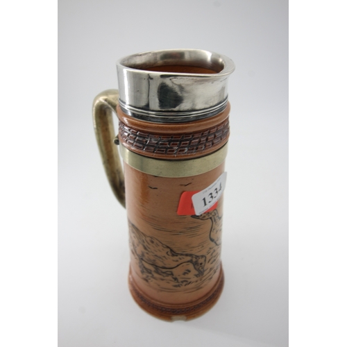 1334 - Doulton stoneware decorative jug having silver rimmed top and brass handle (some damage to base)