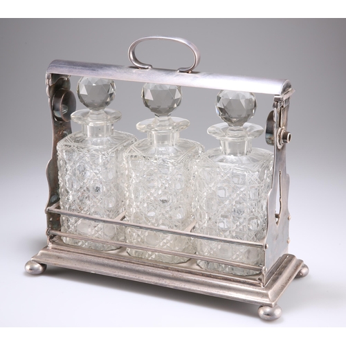 1010 - A LATE VICTORIAN SILVER-PLATED THREE-BOTTLE TANTALUS, with bun feet, the cut-glass decanters of squa... 