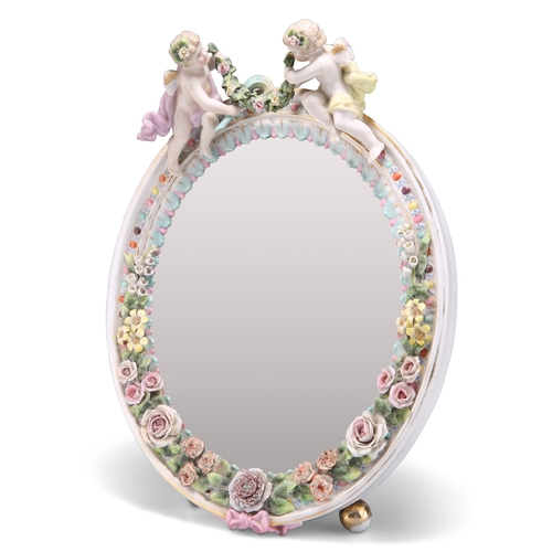 150 - A 19TH CENTURY CONTINENTAL PORCELAIN MIRROR, the floral-encrusted frame surmounted by putti holding ... 