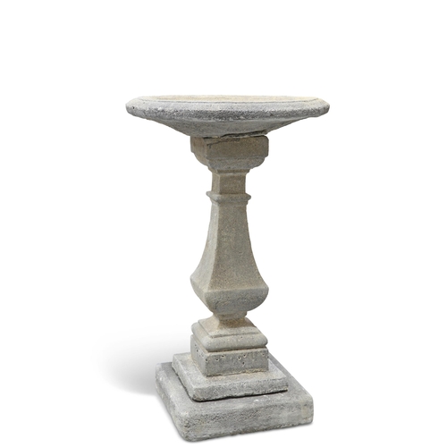 445 - A RECONSTITUTED STONE BIRD BATH, the shallow circular dished top on a shaped square baluster stand. ... 