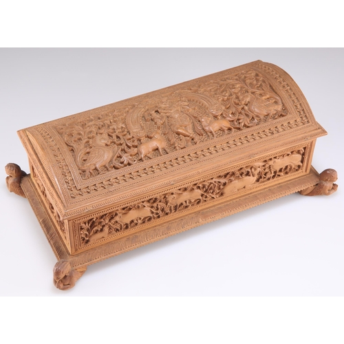 516 - AN INDIAN CARVED SANDALWOOD BOX, rectangular form with a domed casket lid and raised on four angel-f... 