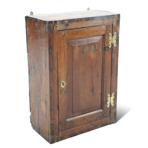 588 - AN 18TH CENTURY OAK CUPBOARD, the panel door with brass hinges. 79cm high, 55cm wide, 29.5cm deep