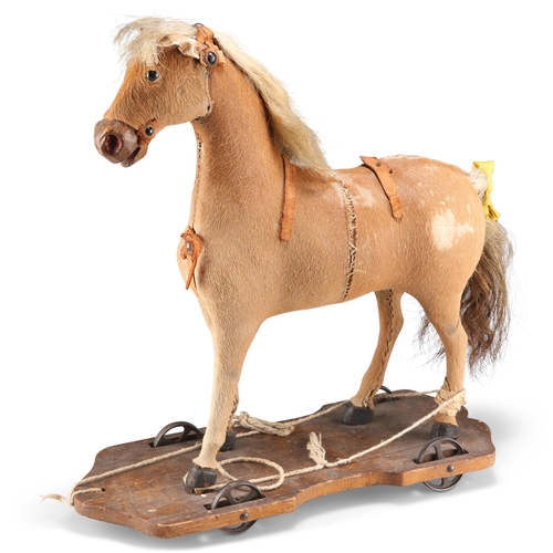 185 - A VICTORIAN PULL-ALONG TOY HORSE, the hide body raised on a wooden stand with metal wheels. 40cm hig... 