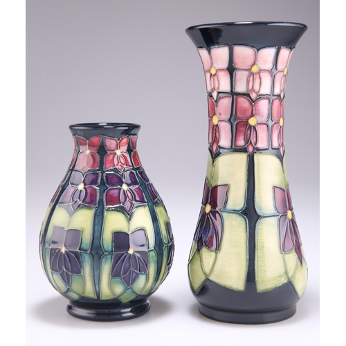 93 - TWO MOORCROFT VIOLET PATTERN TUBE LINED POTTERY VASES, designed by Sally Tuffin, one of trumpet form... 