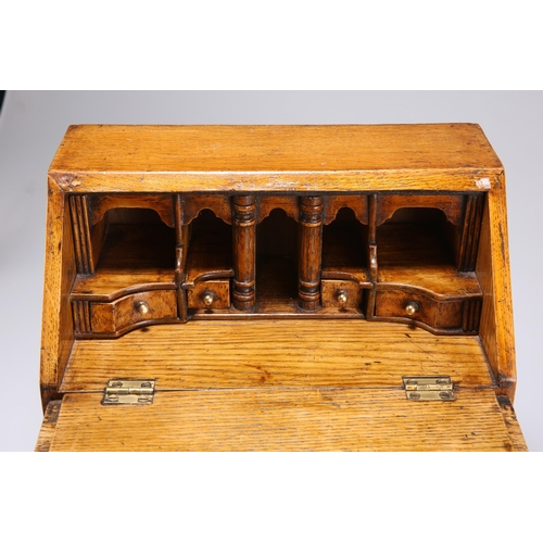 884 - AN 18TH CENTURY STYLE OAK MINIATURE BUREAU with fitted interior and drawer, raised on an integral st... 