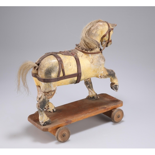 12 - A 19TH CENTURY FOLK ART PULL-ALONG HORSE carved with a raised foreleg, standing on a plinth base wit... 