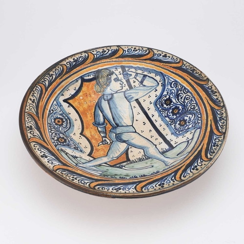 44 - A CONTINENTAL FAIENCE DISH circular, decorated in blue, orange, and green, depicting a figure, the r... 