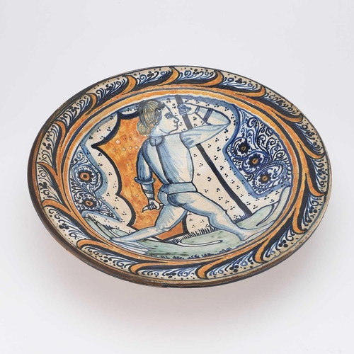 133 - A CONTINENTAL FAIENCE DISH circular, decorated in blue, orange, and green, depicting a figure, the r... 