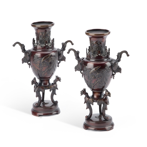 733 - A PAIR OF JAPANESE BRONZE VASES each cast with a phoenix and with bird-form handles, raised on a tri... 