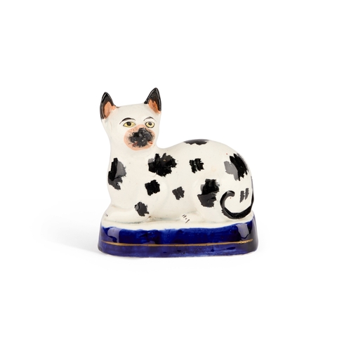 35 - A VICTORIAN STAFFORDSHIRE POTTERY MODEL OF A RECUMBENT CAT, CIRCA 1850 with black markings, on a blu... 