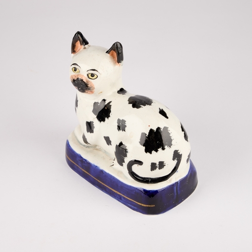 35 - A VICTORIAN STAFFORDSHIRE POTTERY MODEL OF A RECUMBENT CAT, CIRCA 1850 with black markings, on a blu... 