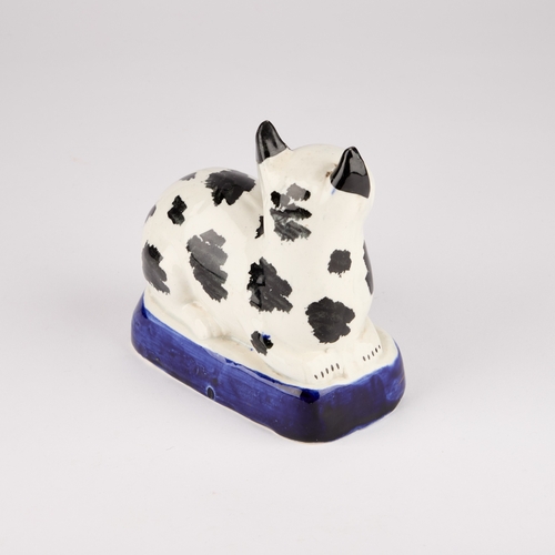 35 - A VICTORIAN STAFFORDSHIRE POTTERY MODEL OF A RECUMBENT CAT, CIRCA 1850 with black markings, on a blu... 