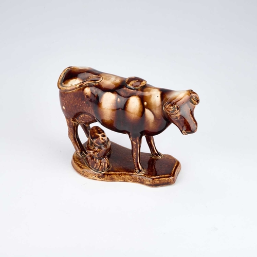 820 - A 19TH CENTURY STAFFORDSHIRE TREACLE-GLAZED POTTERY COW CREAMER AND MILKMAID GROUP modelled as a sta... 