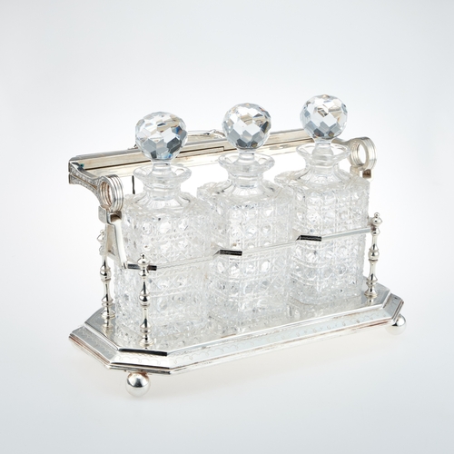 262 - A VICTORIAN SILVER-PLATED THREE-BOTTLE TANTALUS the hinged locking bar with a loop handle with acant... 