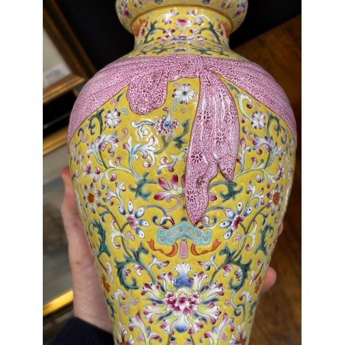 94 - A CHINESE FAMILLE ROSE YELLOW-GROUND VASE of baluster form, moulded with a tied pink swag, bears an ... 